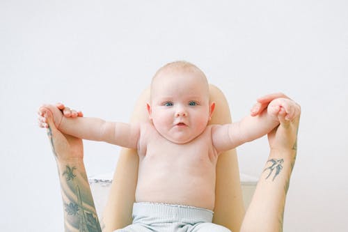 Unrecognizable woman holding baby by hands on knees in light bedroom