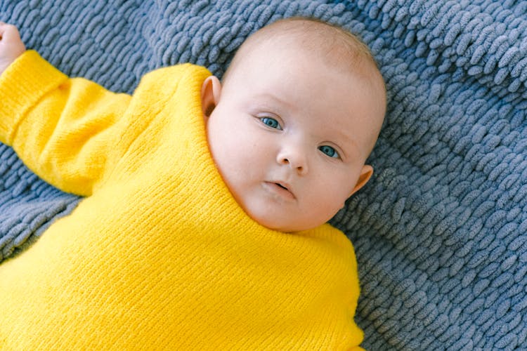 Baby In Yellow Shirt Lying On Grey Textile