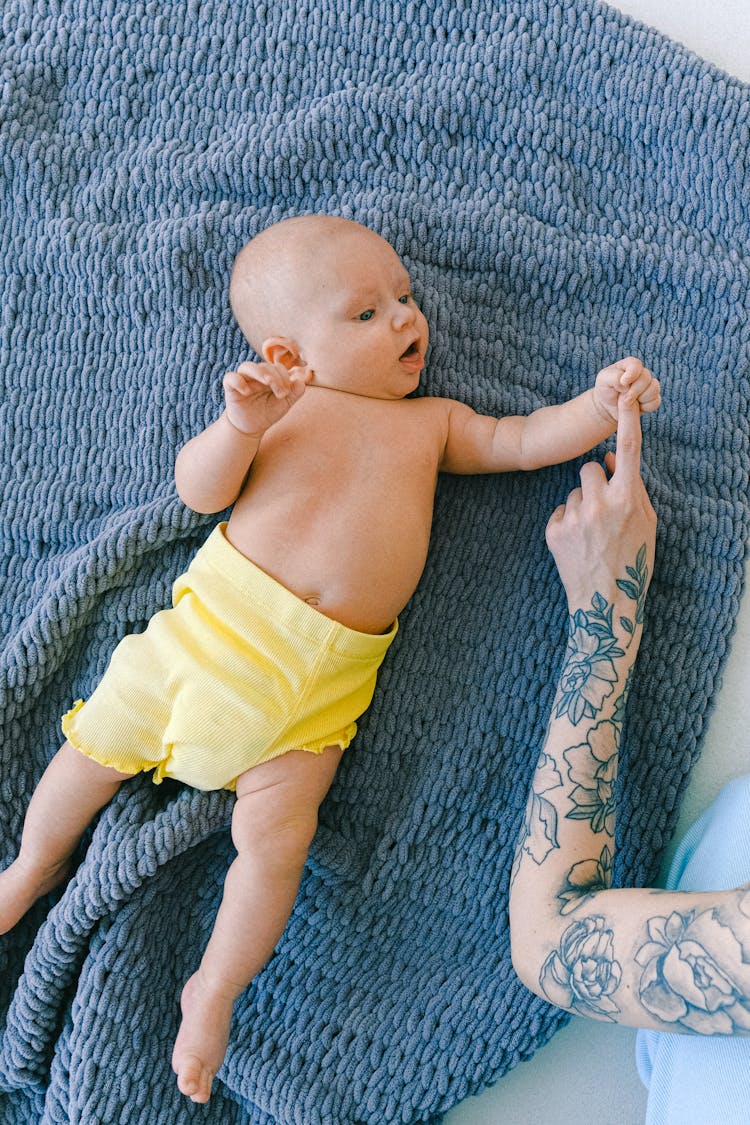 Crop Tattooed Female With Curious Infant Baby Lying On Soft Blanket In Bed