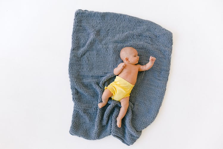 Full Body Of Adorable Newborn Baby Sleeping On Blue Plaid In Studio