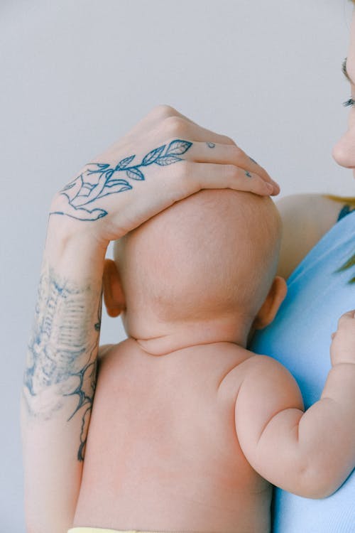 Crop Mère Avec Tatouage Tapotant La Tête Du Nouveau Né Tout En Serrant Le Tout Petit Dans La Chambre