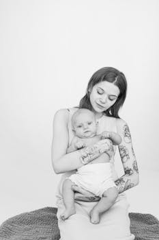 这幅黑白肖像画得温柔，描绘了一位纹身的母亲慈爱地抱着她的孩子