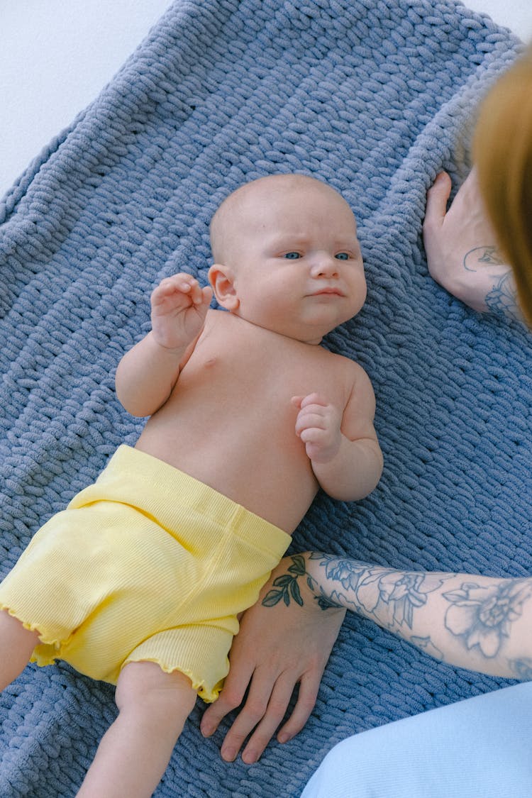 Crop Mother With Cute Newborn Baby Resting On Blue Blanket In Bedroom