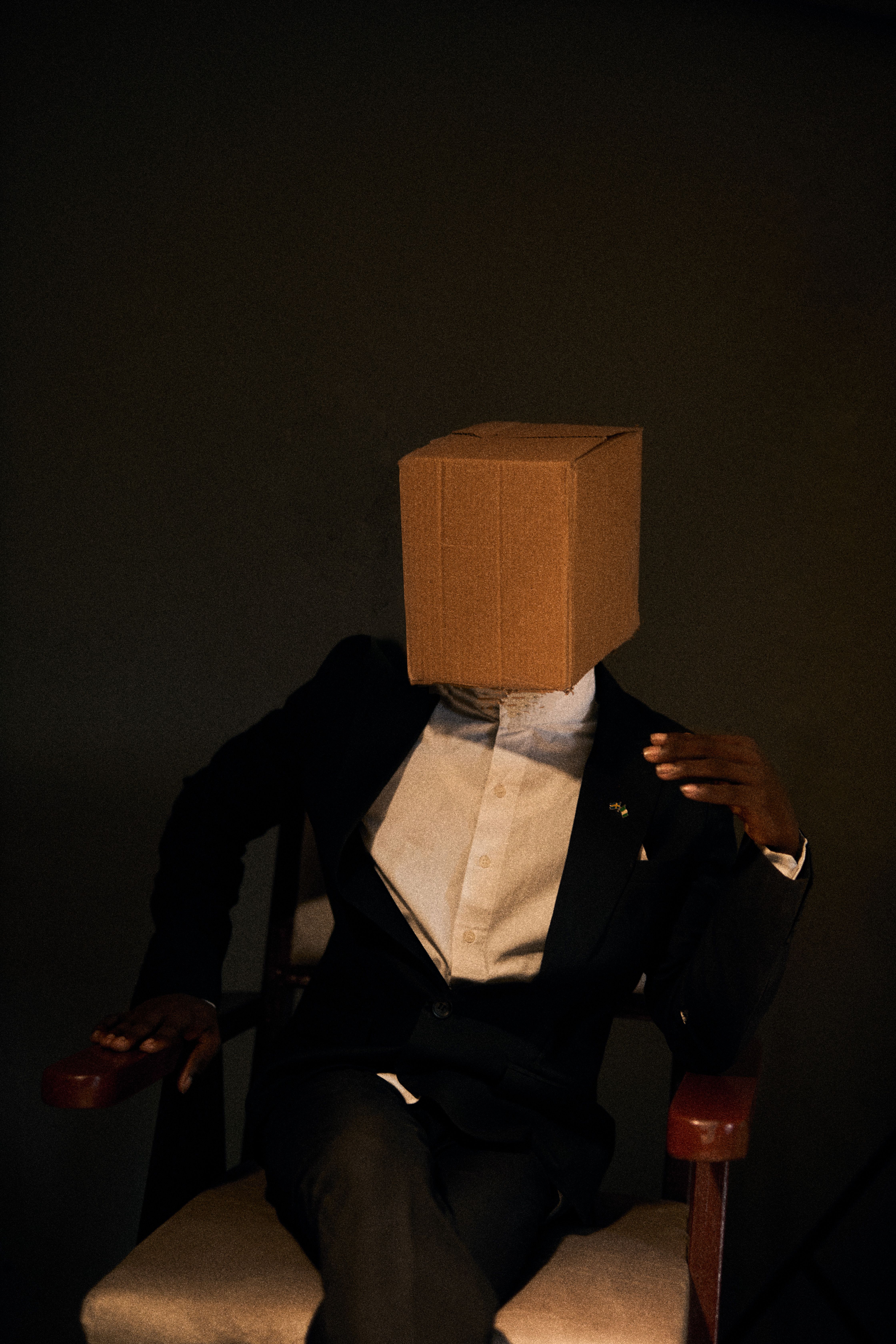 Dark moody portrait of a man in a suit with a cardboard box on his head, representing anonymity.