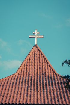 A serene view of a church roof topped with a cross against a clear blue sky.