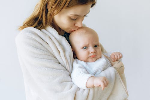 Loving mother hugging and kissing infant in photo studio