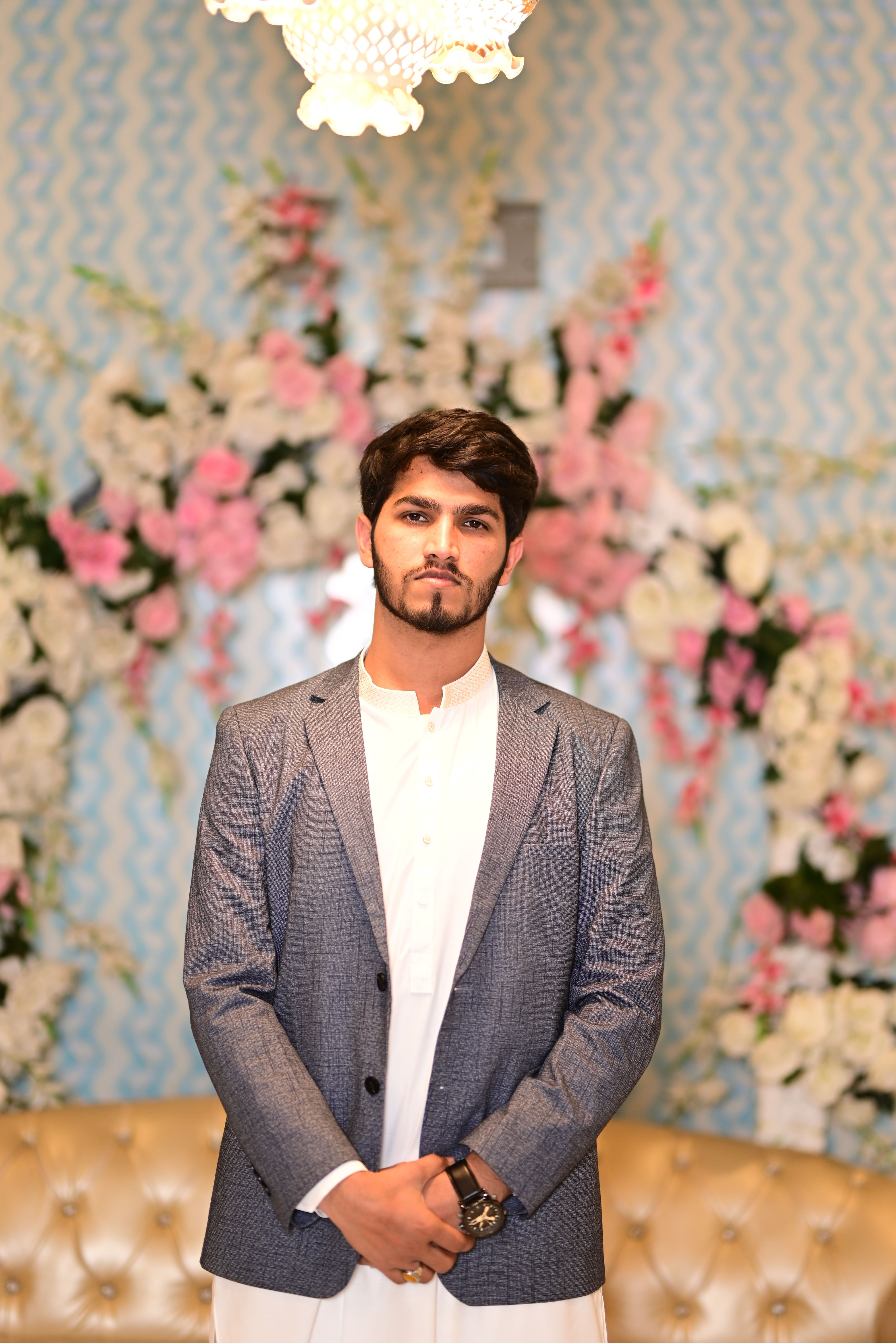 Confident young man in a suit posing indoors with a vibrant floral backdrop, exuding elegance and style.