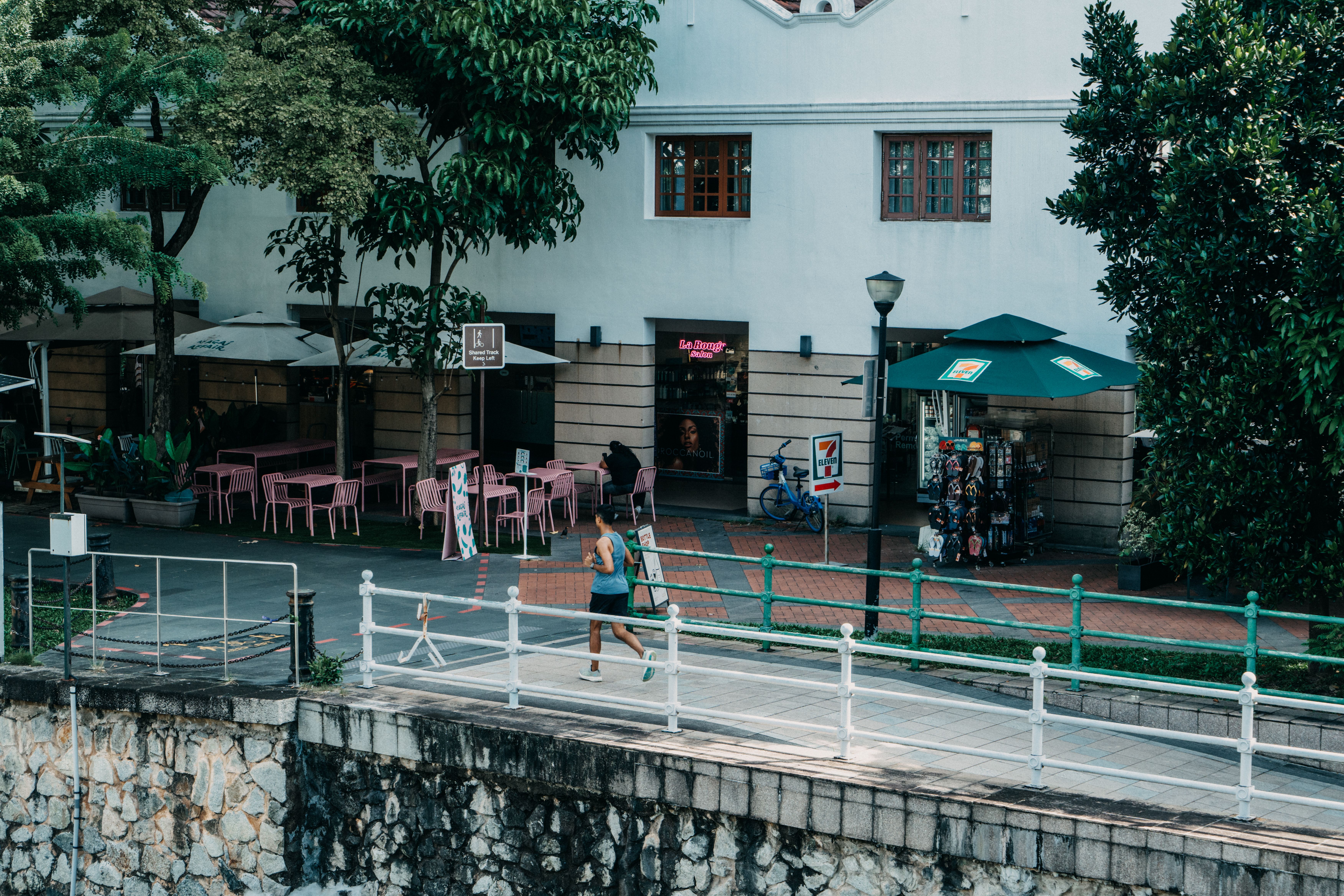 A person jogs along a city street past a café and convenience store, capturing urban lifestyle.
