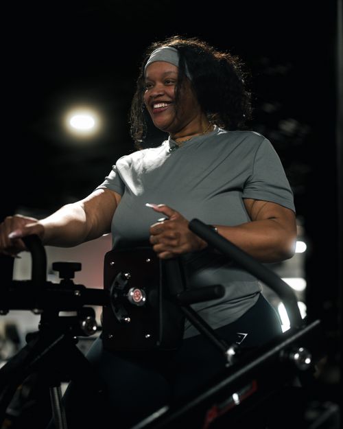 Free Smiling woman engaged in an indoor cycling session, highlighting fitness and positive energy. Stock Photo
