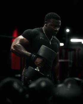 A muscular man lifting dumbbells in a dimly lit gym, showcasing strength and focus.