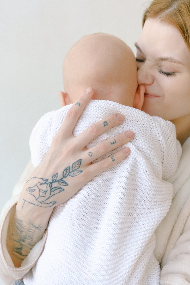 Crop Casual Woman Cuddling With Newborn Child Near Gray Wall In Bedroom