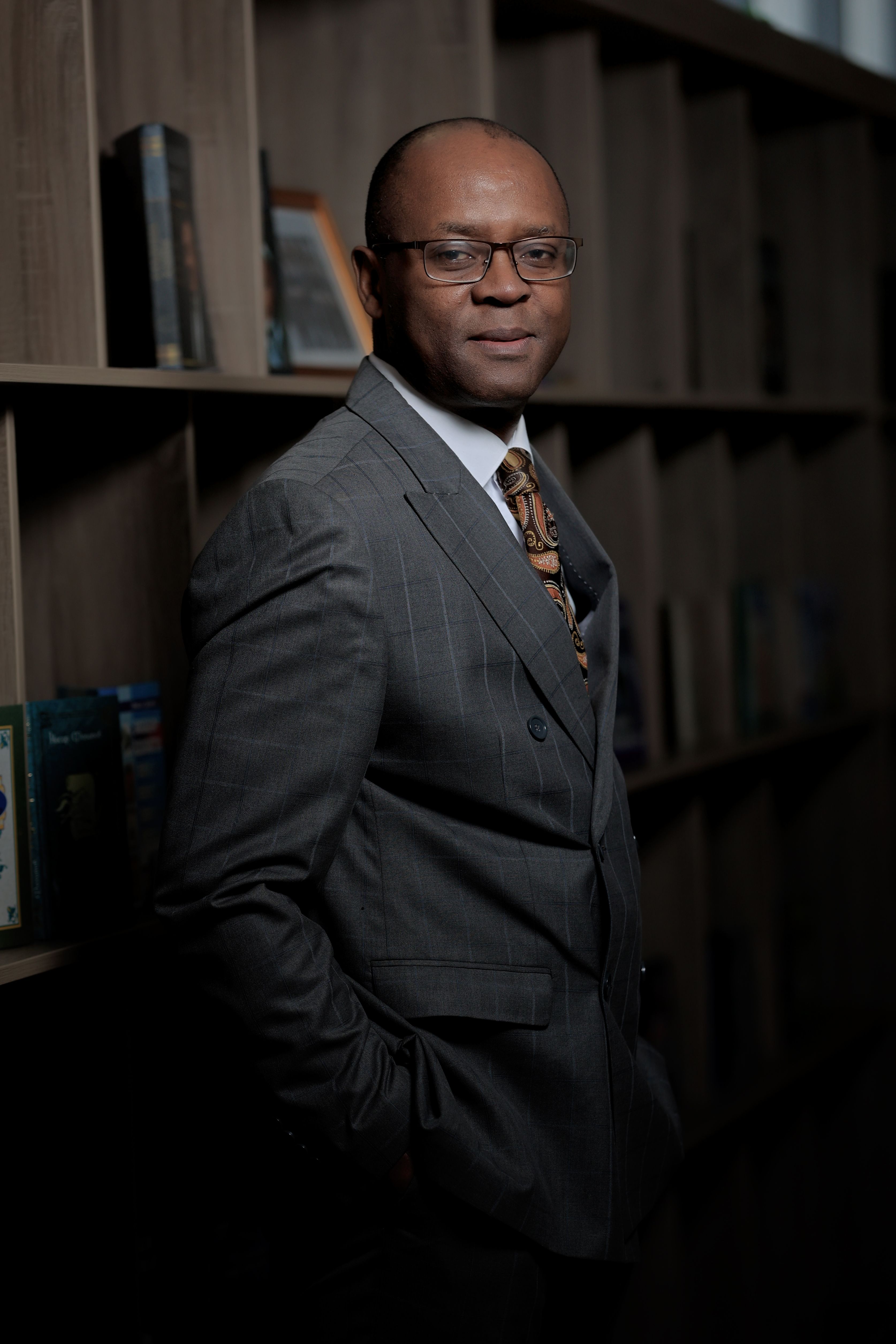A professional businessman confidently posing in a modern office with books.