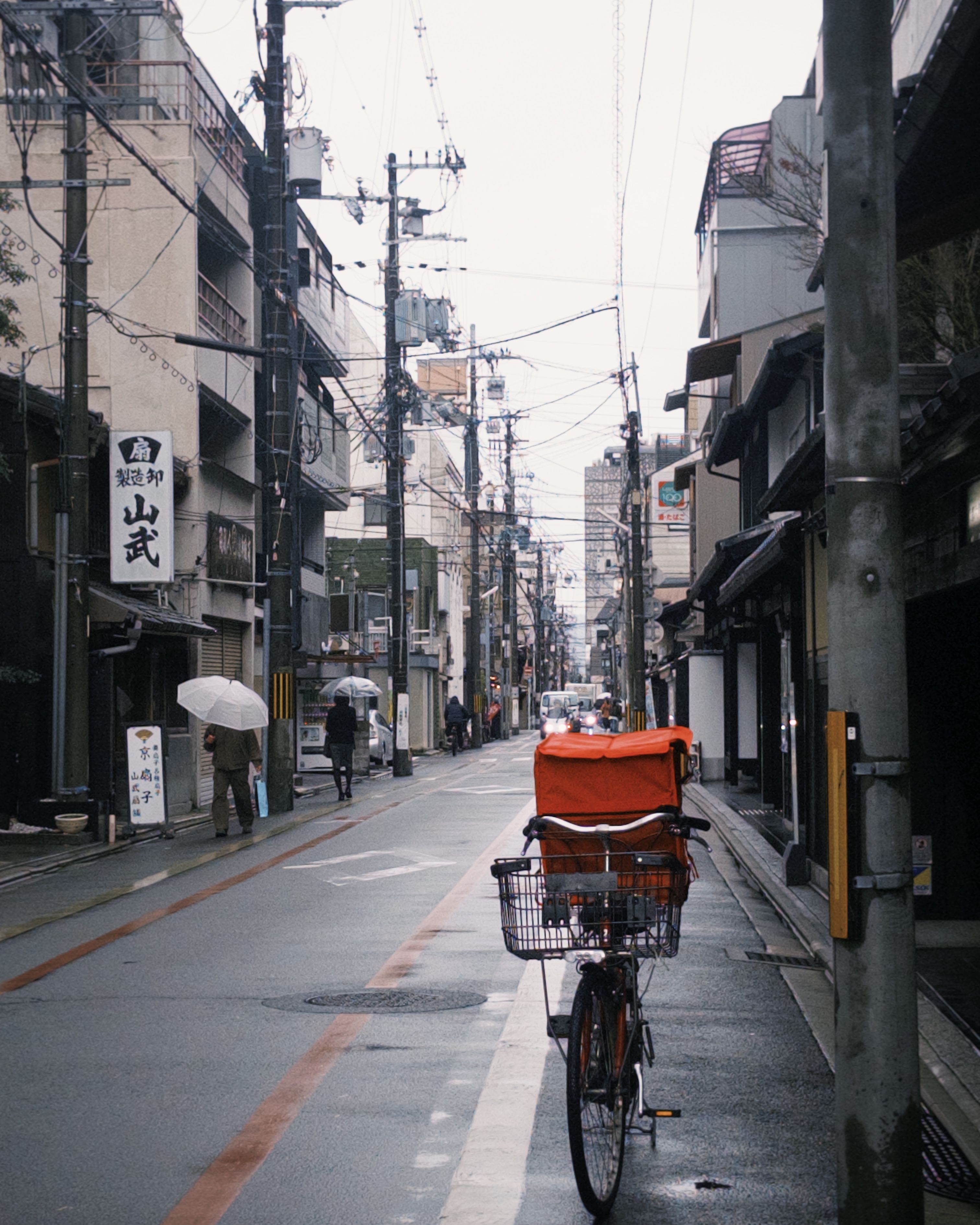 Quiet urban street with bicycle, umbrellas, and buildings on a rainy day, capturing a serene city atmosphere.