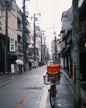Quiet urban street with bicycle, umbrellas, and buildings on a rainy day, capturing a serene city atmosphere.