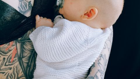 Unrecognizable woman in black underwear embracing newborn baby in knitted overall during afternoon nap in modern studio against black background