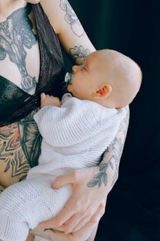 一位母亲纹着身，在安静的室内慈爱地抱着熟睡的孩子