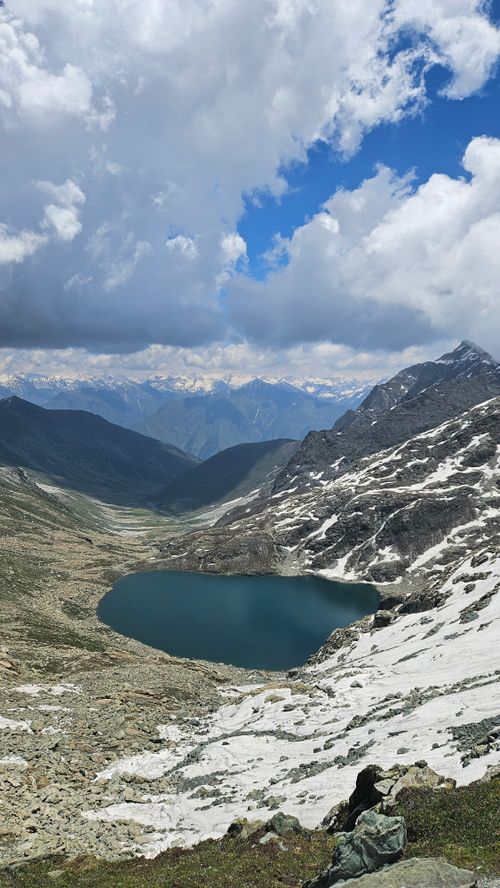 Free Breathtaking view of a mountain lake surrounded by snow-covered peaks under a dramatic sky. Stock Photo