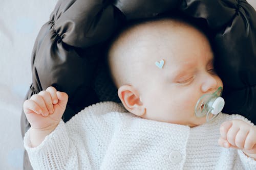 Cute newborn baby with pacifier sleeping on soft cot