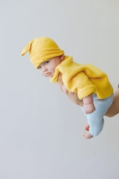 一个穿着黄色针织服装的可爱婴儿在室内摆出俏皮的飞行姿势