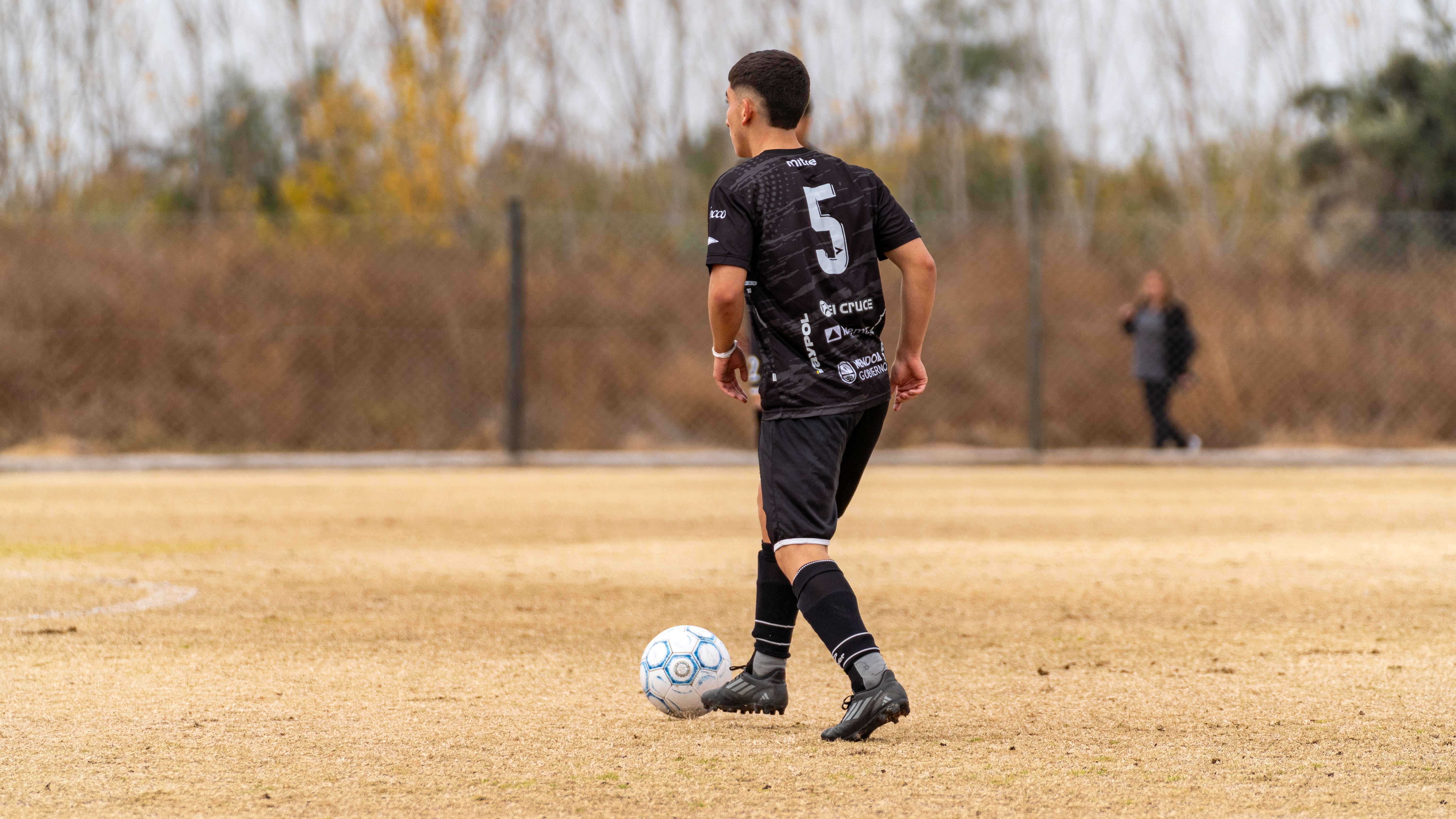 A soccer player in black jersey prepares to pass on an outdoor field.