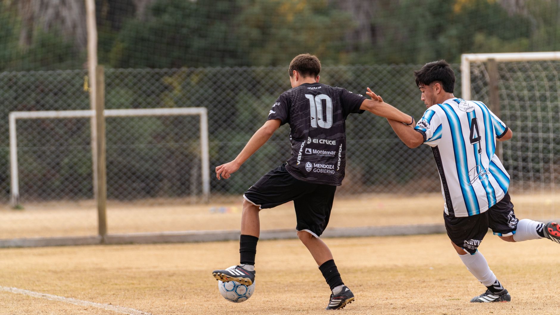 football teammates passing in a triangle while a coach records notes beside a training pitch