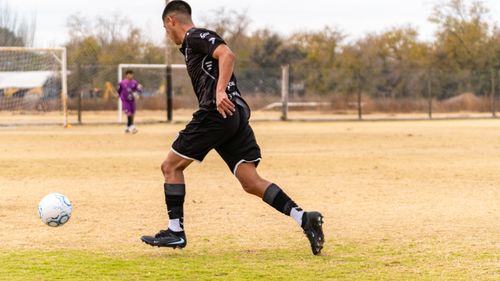 Free Dynamic soccer player in black uniform dribbling on a field during daytime match. Stock Photo