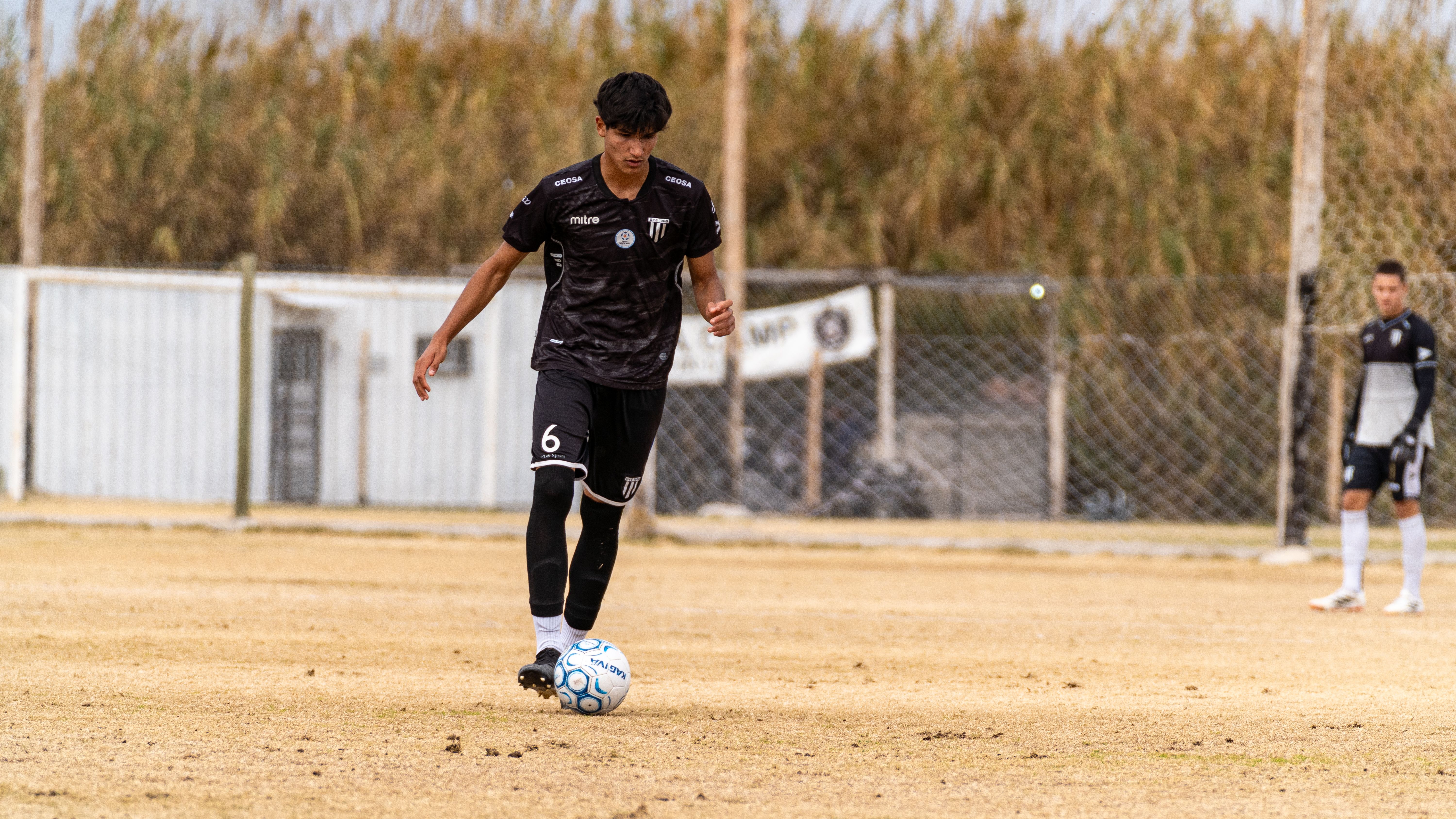 A young male soccer player dribbling a ball on an outdoor field with teammates.