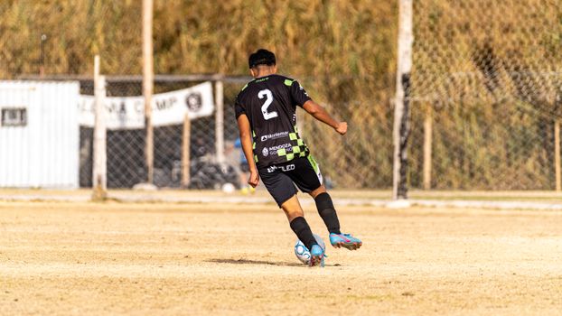 A soccer player takes a shot during an outdoor match on a sunny day.
