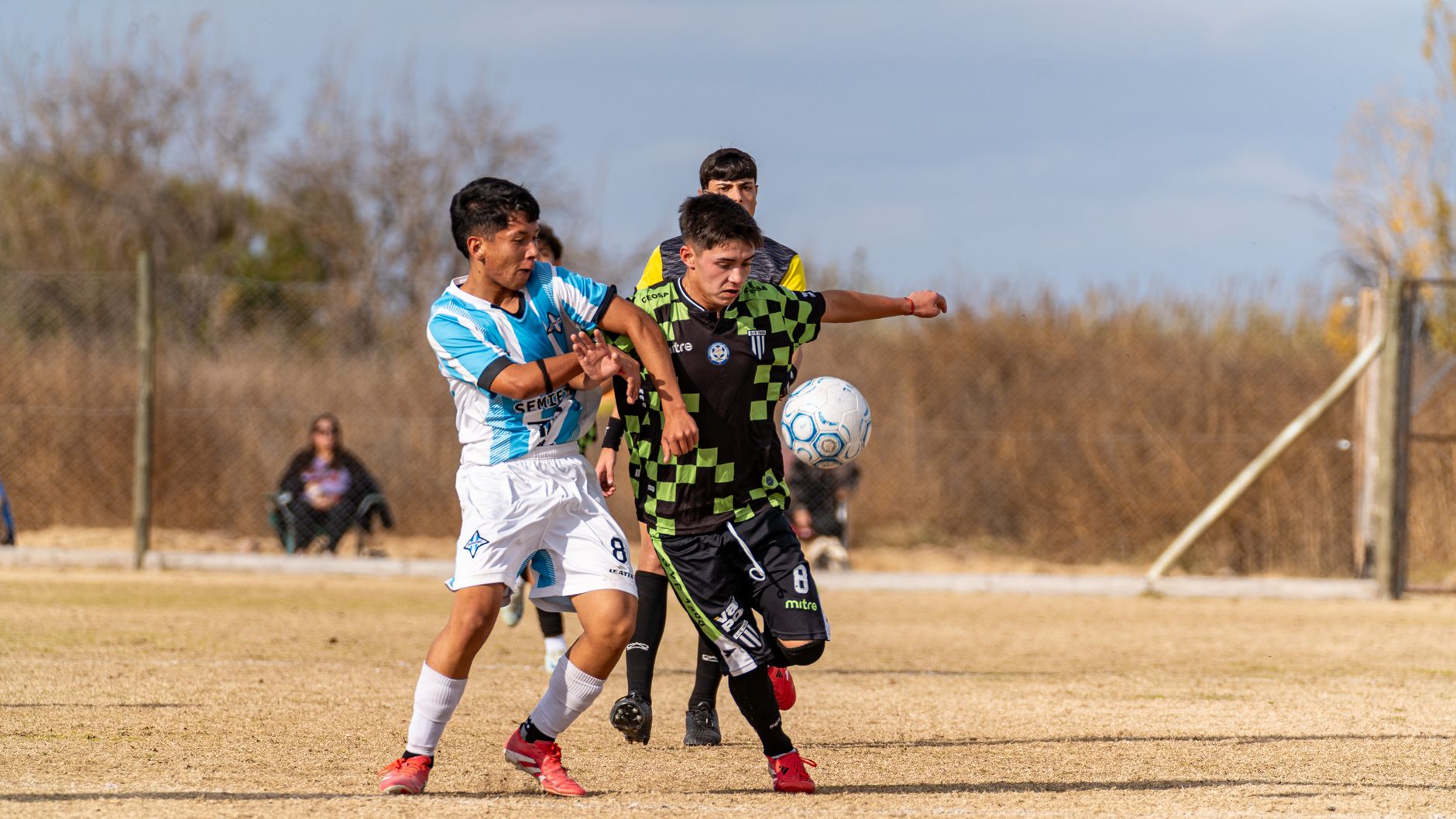 Two youth football players competing for close control inside a marked five-meter square, coach observing