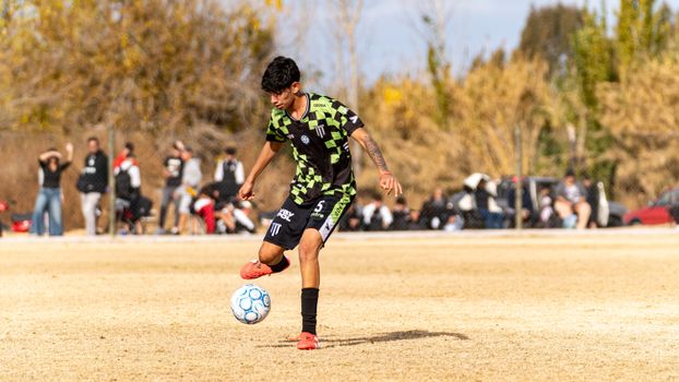 A young soccer player skillfully dribbles the ball on a sunny day field, showcasing agility and focus.