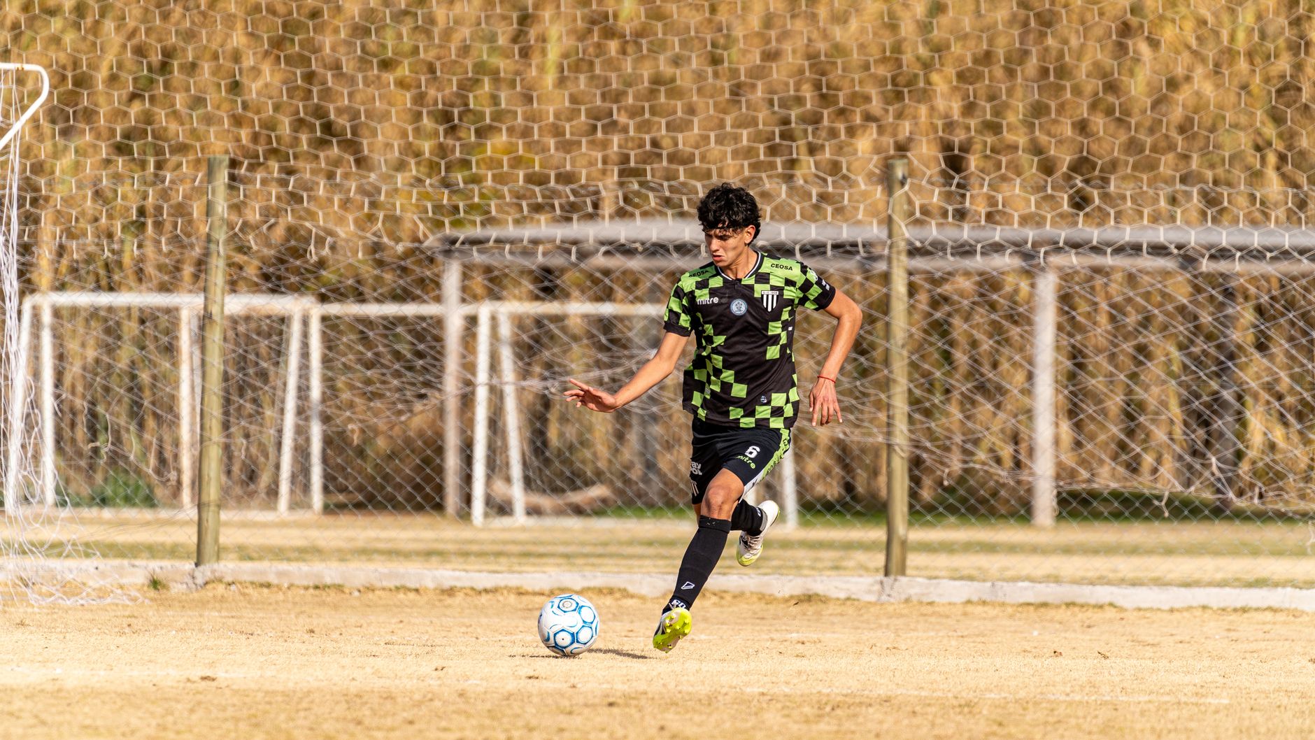 A young male soccer player in action, dribbling the ball on a sunny day on a grassy field.