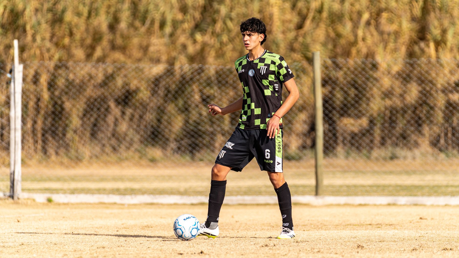 A focused youth football player practicing close control beside cones on a quiet training pitch at sunrise