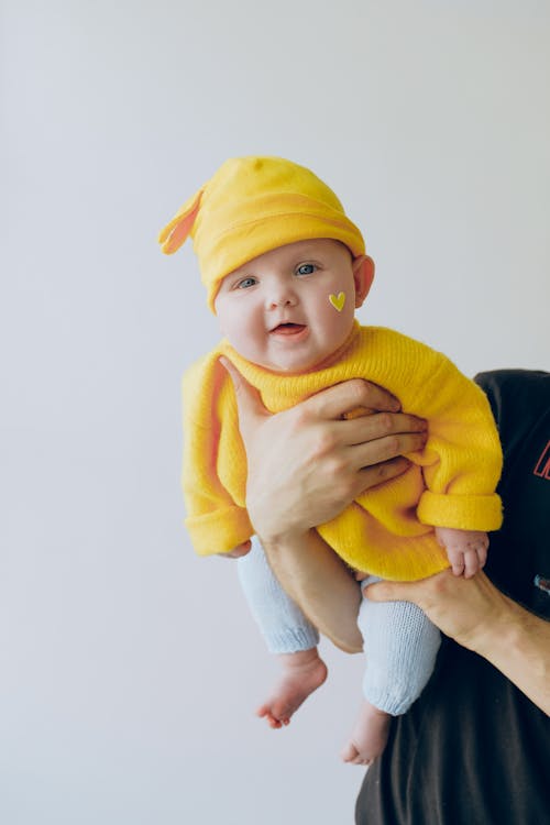 Crop parent holding smiling baby in arms against gray wall in room