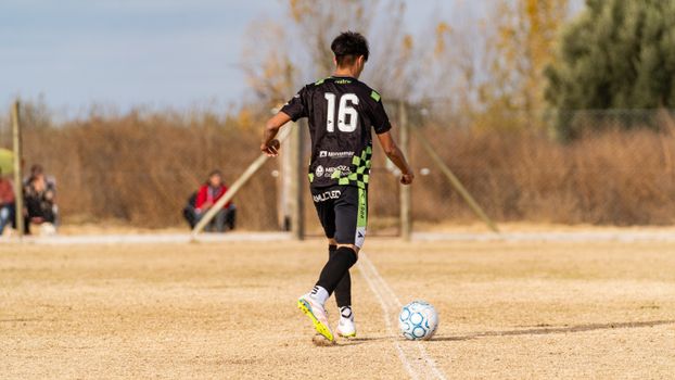 Teenage soccer player with jersey 16 on an outdoor field ready to kick the ball.