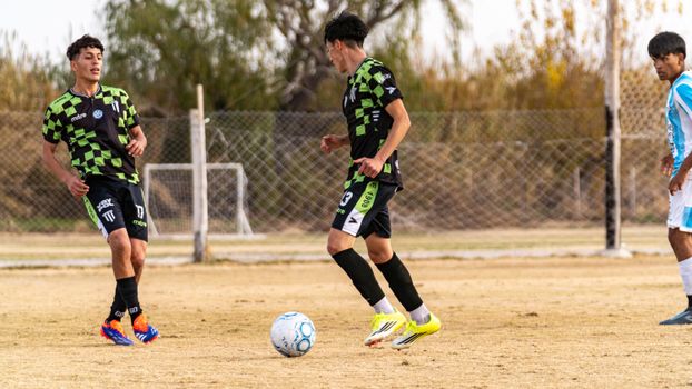 Teenagers playing an outdoor soccer match on a grassy field during the day.