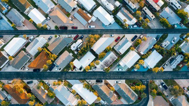 Aerial view of many similar roofs of residential buildings with growing trees and parked cars near narrow asphalt roads in contemporary town in daylight