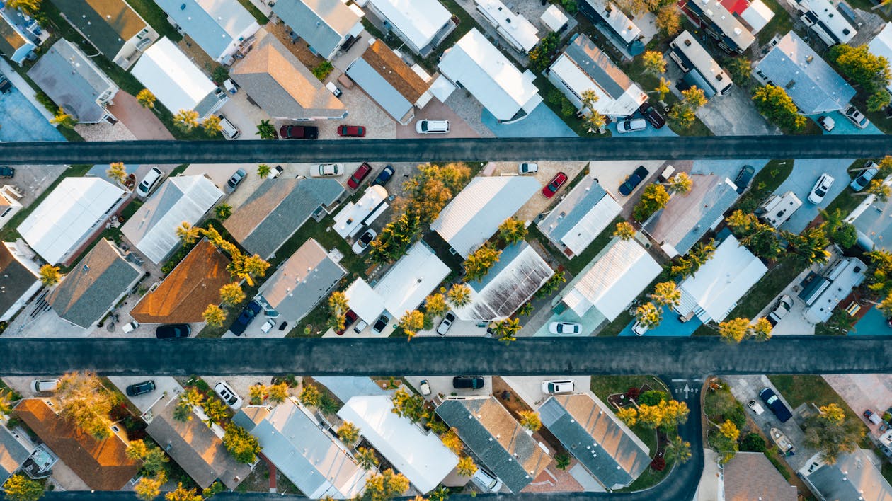 Free Aerial view of many similar roofs of residential buildings with growing trees and parked cars near narrow asphalt roads in contemporary town in daylight Stock Photo