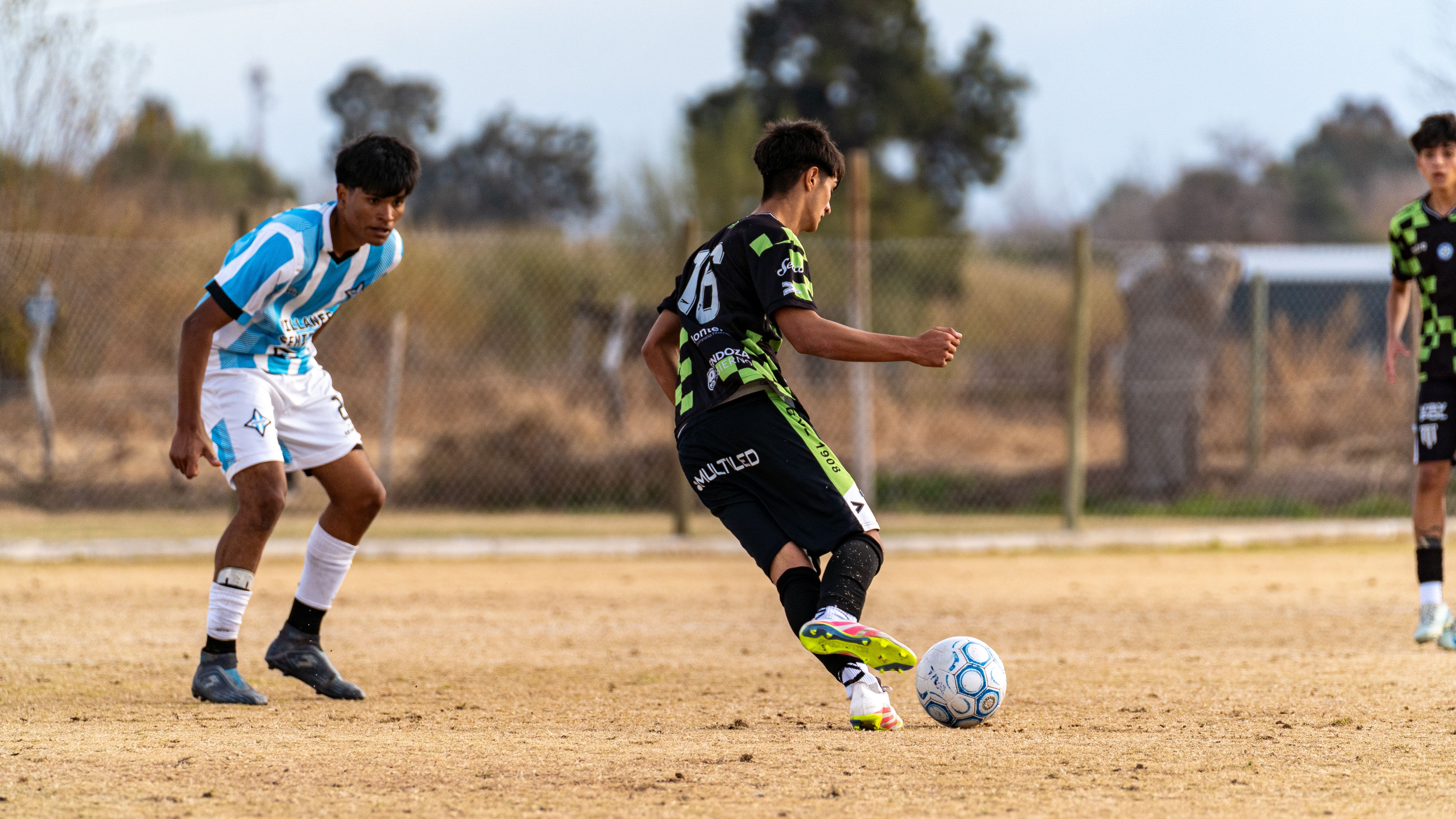 Teenagers playing a competitive soccer match outdoors on a grass field during the day.