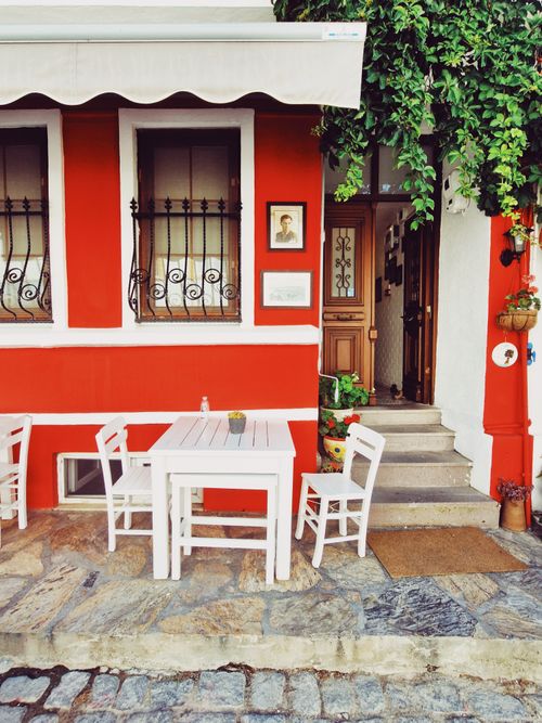 Free Inviting cafe setting outside a vibrant red building in Bozcaada, Turkey. Stock Photo