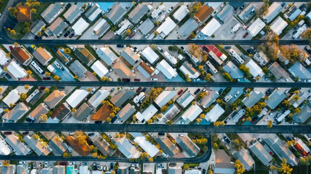 Overhead view of roofs of dwelling houses near growing trees and parked vehicles with narrow horizontal asphalt roads in modern suburb