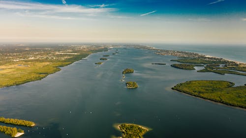 Drone view of picturesque green islands with growing trees surrounded by endless ocean under blue sky with clouds in summer