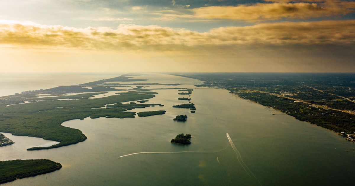Drone view of spectacular green islands surrounded by serene endless sea with horizon line under colorful cloudy sky at sundown