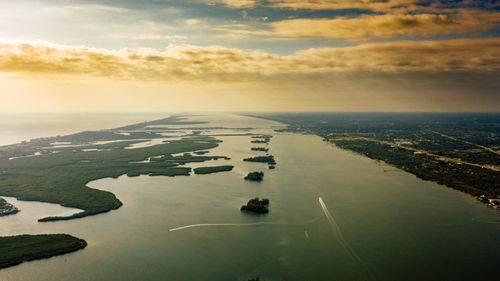 Free Drone view of spectacular green islands surrounded by serene endless sea with horizon line under colorful cloudy sky at sundown Stock Photo