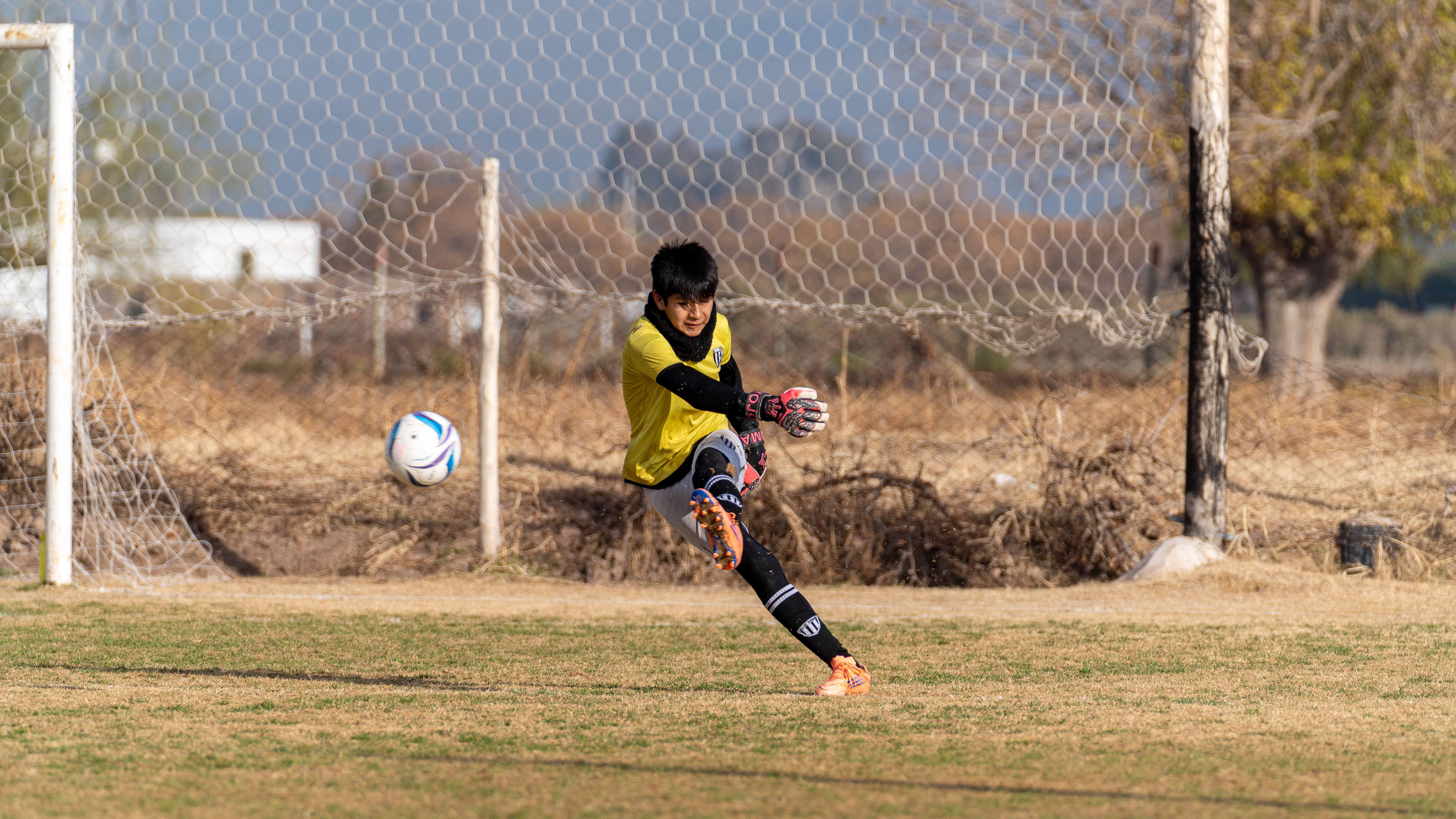 A youth soccer goalkeeper making a precise kick during a game outdoors on a sunny day.