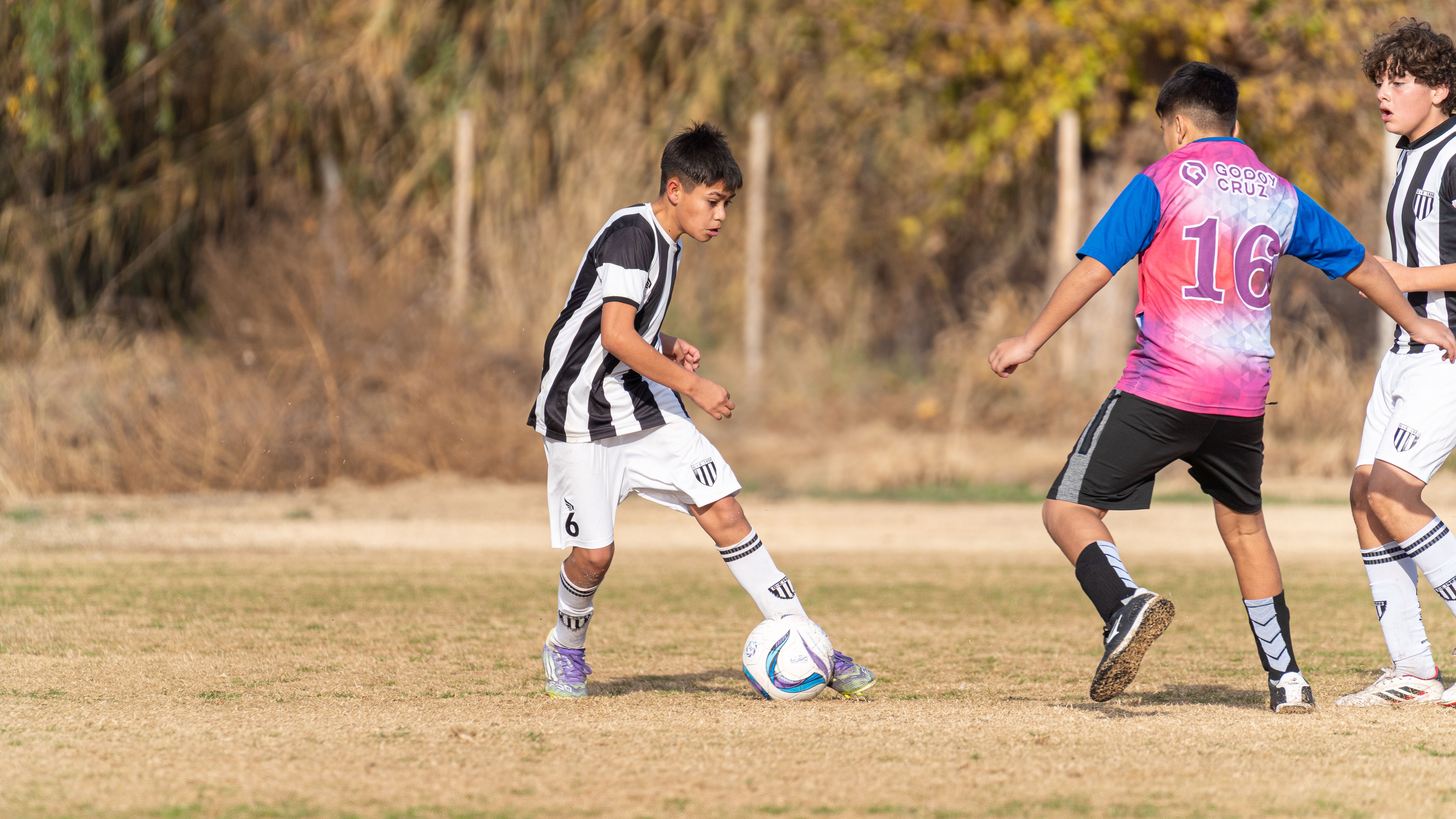 Three boys playing soccer outdoors on a sunny day.