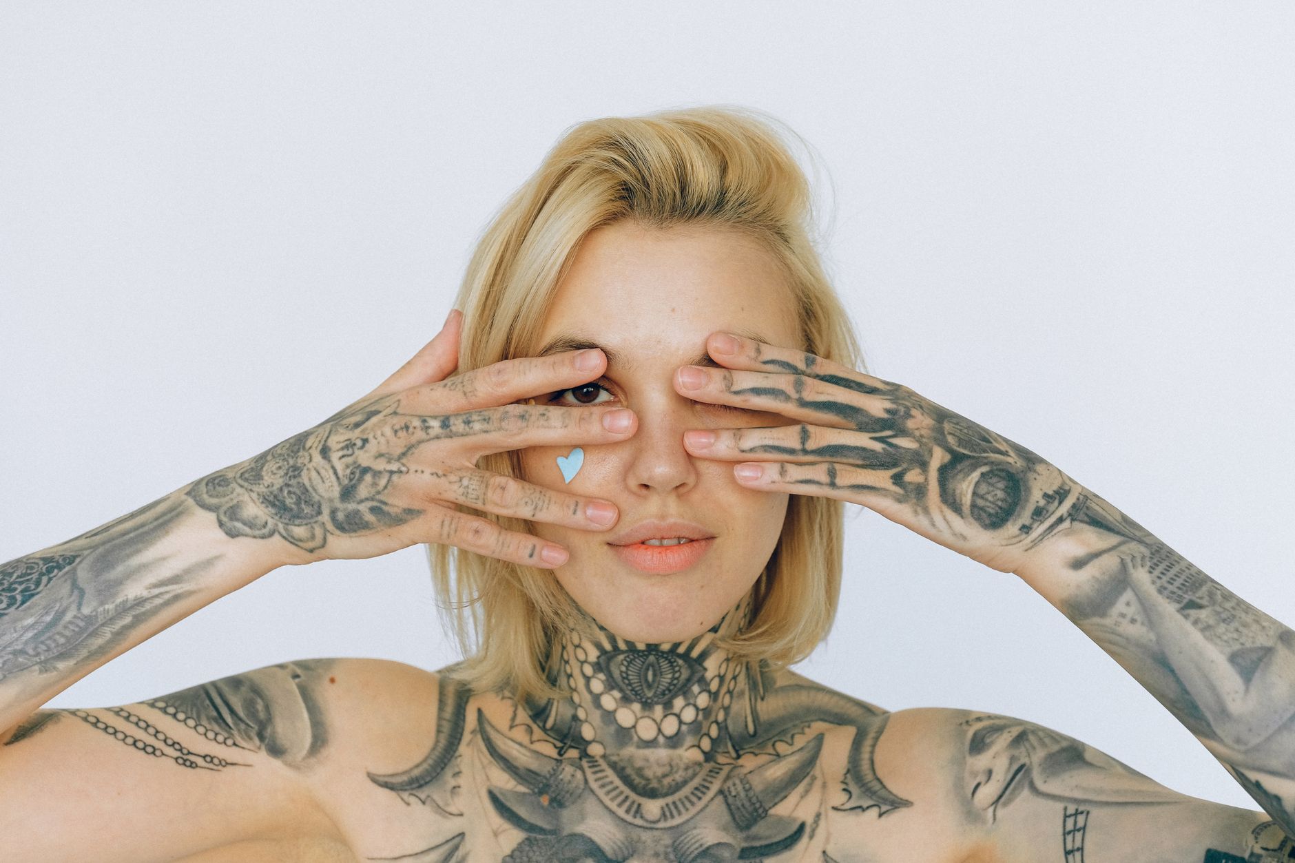 청년지원금 외 대체 지원금 5유형 비교 정리 3 Positive tattooed blond woman looking through fingers at camera while standing against gray background in modern studio