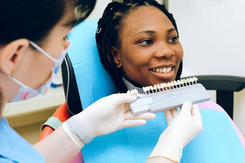 Cheerful black woman sitting in dental chair of modern dentist office and checking teeth implant while looking away