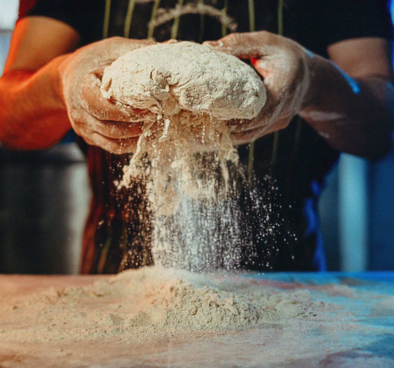 A baker works by hand with flour and dough, creating artisanal bread in an industrial kitchen.