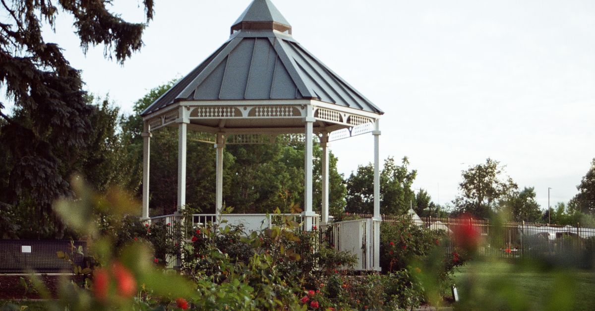 Scenic view of a quaint gazebo surrounded by lush roses in a serene park setting in Littleton, Colorado.