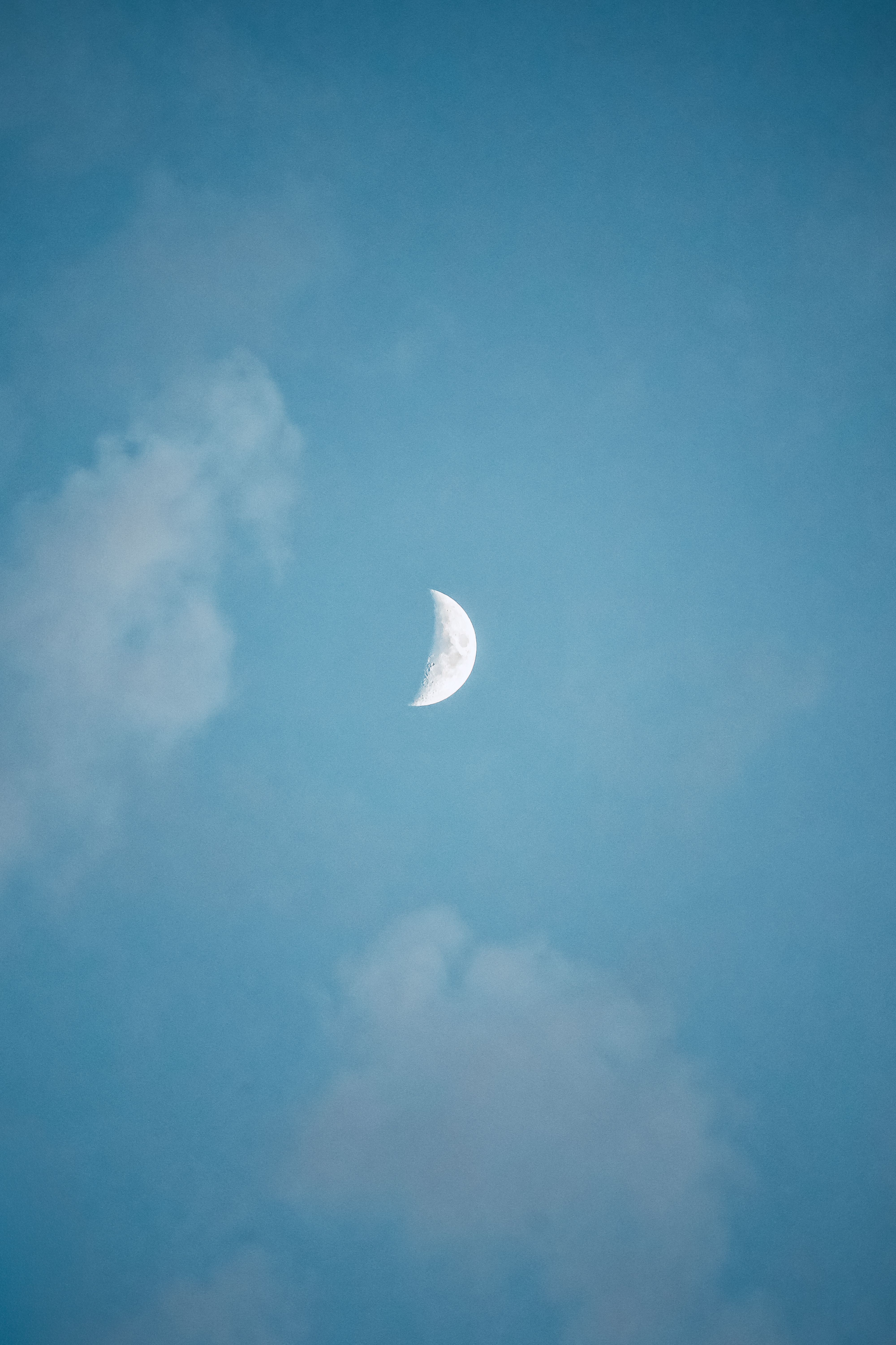 A serene crescent moon amidst a soft blue sky and gentle clouds.
